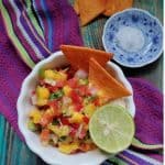 Bowl of fresh mango salsa with diced mango, tomato, onion, and red bell pepper garnished with coriander leaves.