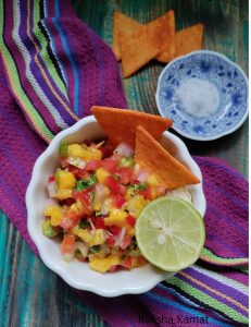Bowl of fresh mango salsa with diced mango, tomato, onion, and red bell pepper garnished with coriander leaves.