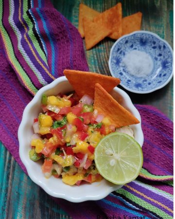 Bowl of fresh mango salsa with diced mango, tomato, onion, and red bell pepper garnished with coriander leaves.