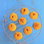 Baked Nankhatai cookies cooling on a wire rack with a traditional Indian teapot nearby.