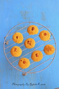Baked Nankhatai cookies cooling on a wire rack with a traditional Indian teapot nearby.