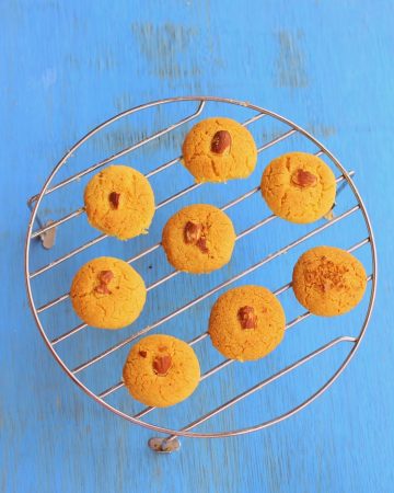Baked Nankhatai cookies cooling on a wire rack with a traditional Indian teapot nearby.